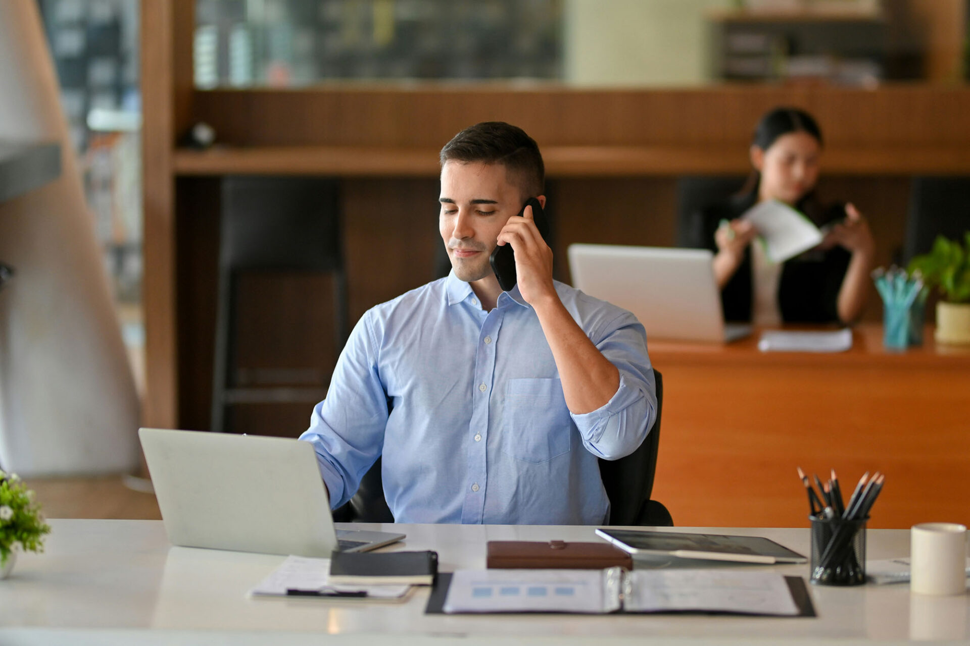 Finance professional on business call while working on account reconciliation tasks at laptop with documents in office