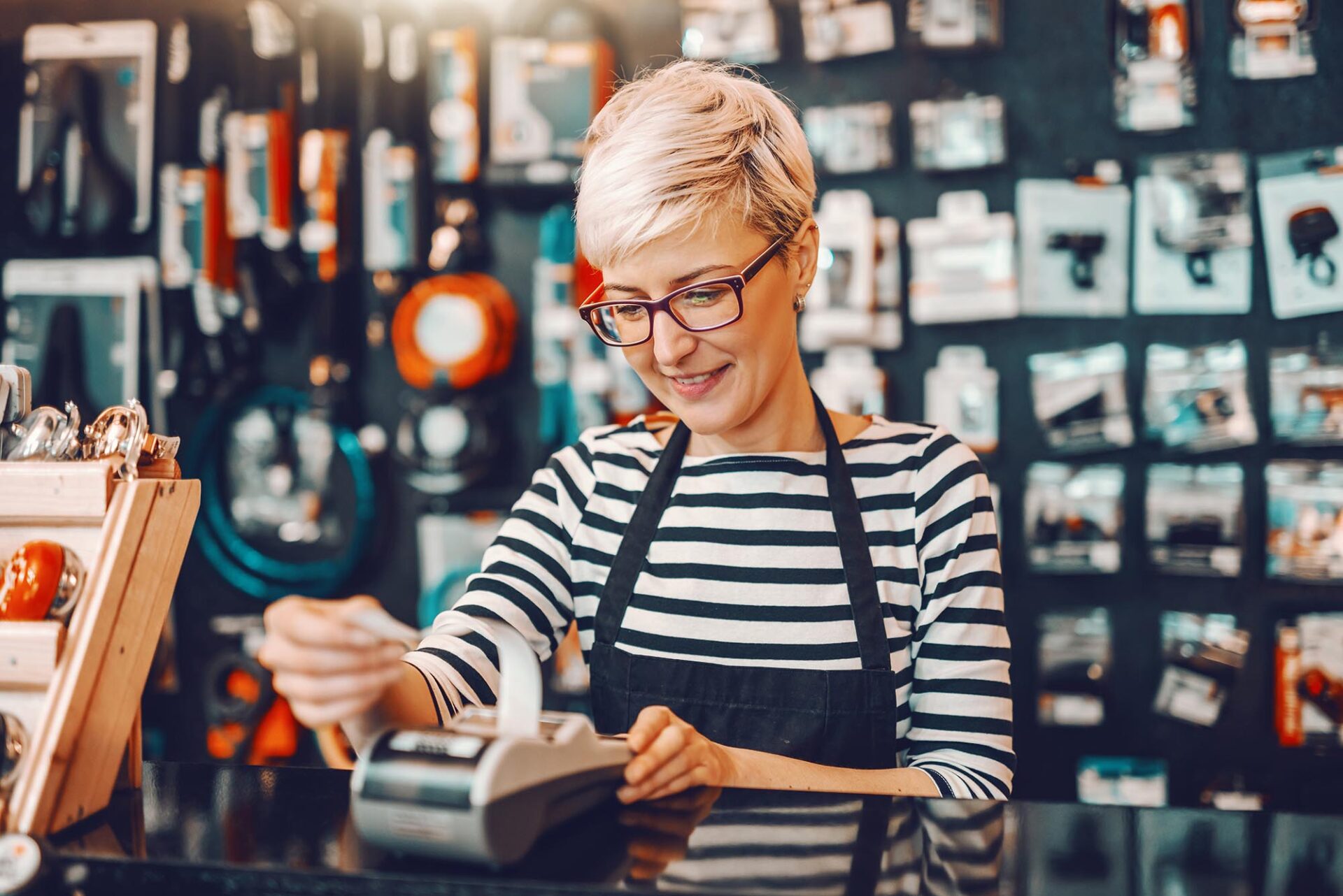 Retail worker using card machine while reviewing account reconciliation software tasks at counter